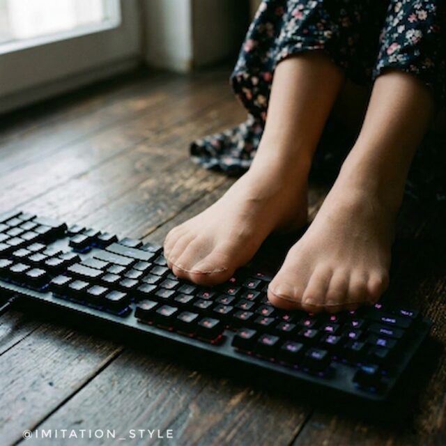 肌色パンストを履いた足がゲーミングキーボードのホームポジションに乗っている